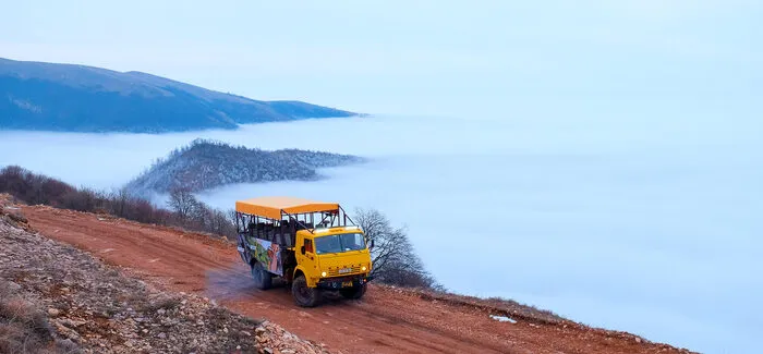 Off-road truck on a mountain ridge above a sea of clouds